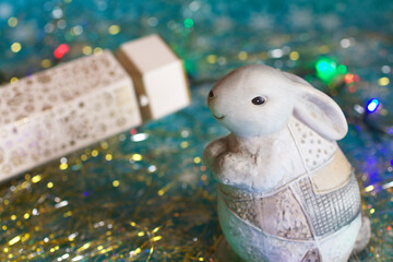 Closeup of cute rabbit with a white cracker on a golden tinsel. A symbol of new year 2023 with a colorful garland. Christmas decorations, winter holidays concept background