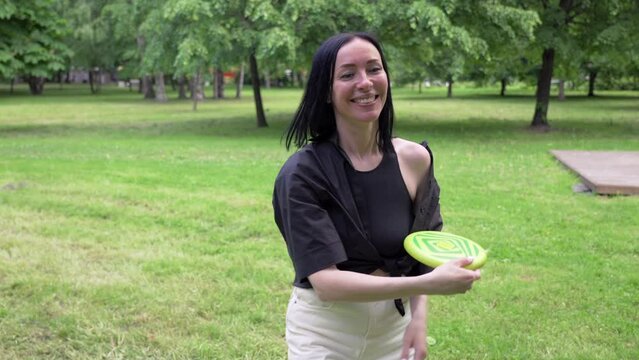 Near angle young smile woman with black hair plays frisbee in the park on a summer day