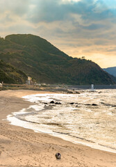 Breaked Plastic buoy stranded on the Sunset Beach leading to the famous Sakurai Futamigaura's Couple Stones protected by a sacred white Shinto torii gate in Fukuoka at dusk with moutain in background.
