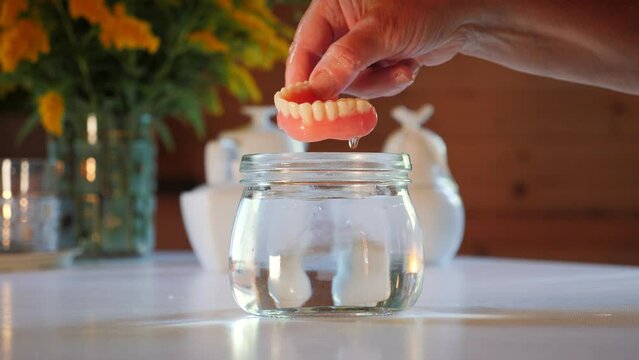 Taking false teeth out of glass of water. Elderly female hand takes dentures out