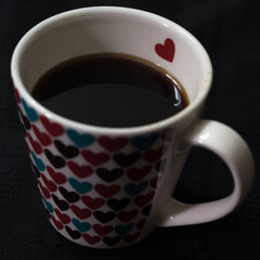 Taza de cafe, taza blanca con corazones de colores con cafe sobre fondo oscuro