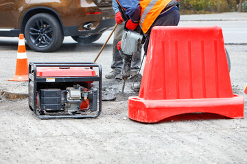 Road workers are repairing the carriageway of a section of the road with an electric jackhammer fenced with a red road shield.