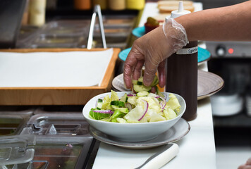 Kitchen employee preparing salad for customer food order