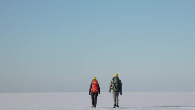 The two people with backpacks walking through the snow field. slow motion