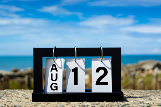 Aug 12 calendar date text on wooden frame with blurred background of ocean.