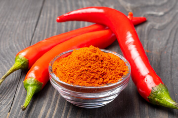 chili peppers on wooden table and ground pepper in small bowl