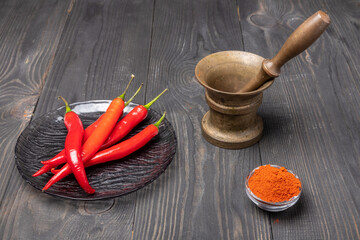 raw and ground chili peppers and a mortar on wooden background