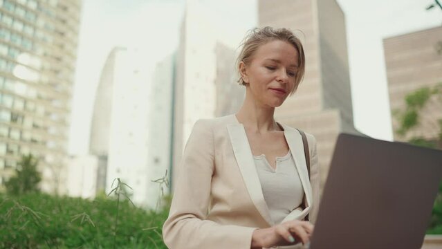 Businesswoman with blond hair wearing beige suit is using pc laptop outside