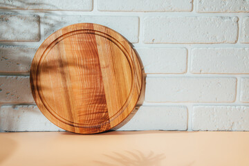 Wooden round board on orange table with shadow from palm tree with free space for inscription in a...