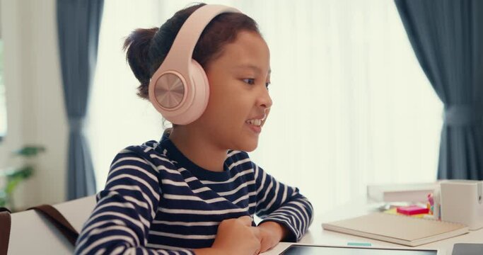 Asian toddler girl with sweater wear headphone sit front of desk with notepad use magic pen focus on writing do homework, finger counting number math online learning course from laptop at home.