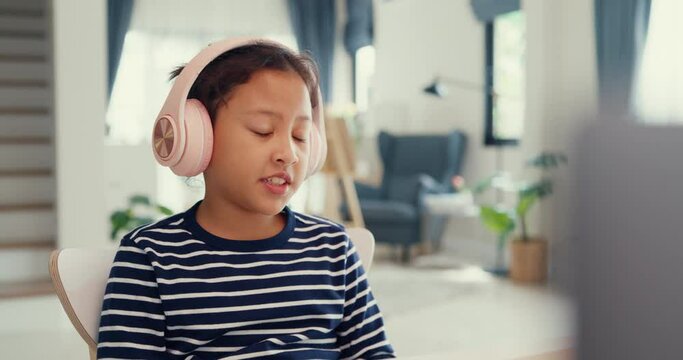 Asian toddler girl with sweater wear headphone sit front of desk with notepad use magic pen focus on writing do homework, finger counting number math online learning course from laptop at home.