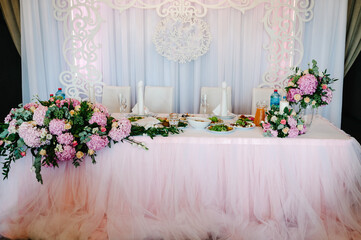 Festive table, arch decorated with composition of violet, purple, pink flowers and greenery, candles in the banquet hall. Table newlyweds in the banquet area on wedding party.