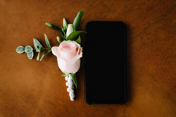 Black smartphone with a clear blank screen on a brown background. Flat lay. Top view. Phone with an empty screen with pink rose, space for your application text, holiday present greeting concept.