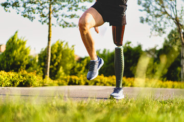 Crop view of disabled athlete man with prosthetic artificial leg exercising outdoors in the parkland - health and people lifestyle concept - obrazy, fototapety, plakaty