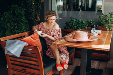 Outdoor fashion portrait of a stunning woman sitting in a cafe. I drink coffee and read an old book. a woman in a dress and a hat.