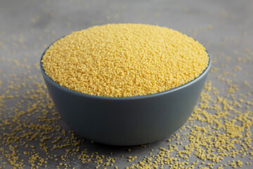 Raw organic couscous in a bowl on a gray surface, side view.