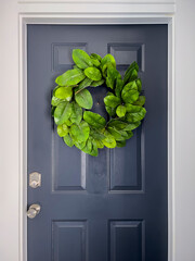 Front view of a navy blue door with a colorful green wreath on a bright, sunny day