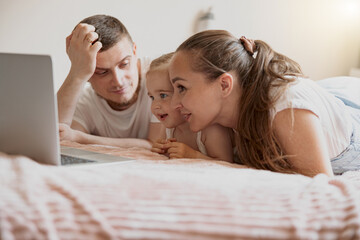 Cheerful family having fun together watching cartoons online on laptop lie on sofa at home