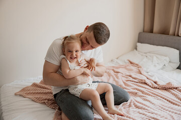 Daddy playing with dauther at home sitting on the bed