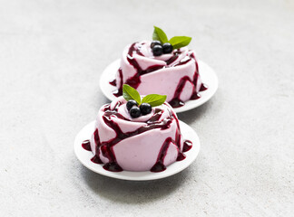 Vegan dessert. Black currant cream pudding, Panna Cotta with sauce, in the shape of a rose, on a plate. Light grey background