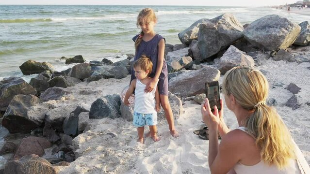 Mom photographs daughter with her brother on the phone on the beach near the sea