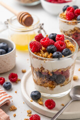 Granola with yogurt in glass served with fresh raspberry, blueberry and honey. Homemade oatmeal muesli. Vegetarian breakfast, healthy eating concept. Selective focus.