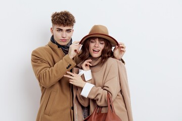 a cute couple is standing on a white background, wearing a coat. A man pulls a hat on a woman's head, and she holds her joined hands in front of her