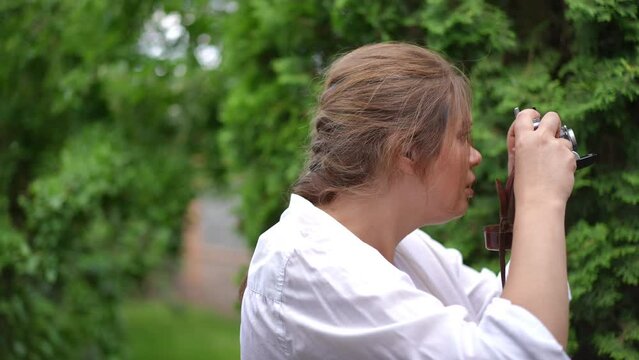 Side view curios talented plus-size woman taking photos of summer nature in green garden outdoors. Happy confident Caucasian photographer photographing trees in park in slow motion smiling
