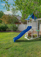 Vertical Whispy white clouds Small set of playground on a green lawn at the fenced backyard a