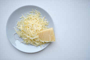 Plate with grated hard delicious cheese on a light background. Dairy. Concept: Italian cuisine, cheese, restaurant and food. copy space