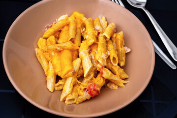 Penne with tomato and bacon in egg creamy sauce on beige plate, appetizer.