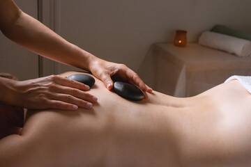 SPA procedure in a massage room with the help of hot stones, two hands of a woman masseur on the female patient's body