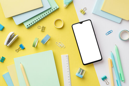 Back to school concept. Top view photo of smartphone diaries sharpener ruler pens binder clips adhesive tape and stapler on bicolor yellow and white background with empty space
