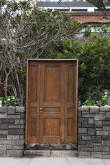 Fototapeta na wymiar Puerta de madera color marrón junto a un cerco de piedras.