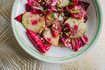 radicchio salad with watermelon radish, blood orange, pistachios on white plate with green greek key