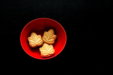 Delicious cookies filled with vanilla cream made with honey or maple syrup from Canadian trees, the traditional sweet of Canada in a red bowl of heart shape on a black background