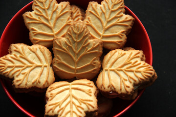 Delicious cookies filled with vanilla cream made with honey or maple syrup from Canadian trees, the traditional sweet of Canada in a red bowl of heart shape on a black background