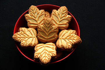 Delicious cookies filled with vanilla cream made with honey or maple syrup from Canadian trees, the traditional sweet of Canada in a red bowl of heart shape on a black background