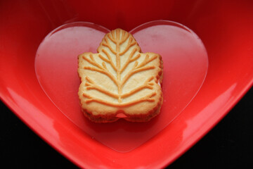Delicious cookies filled with vanilla cream made with honey or maple syrup from Canadian trees, the traditional sweet of Canada in a red bowl of heart shape on a black background