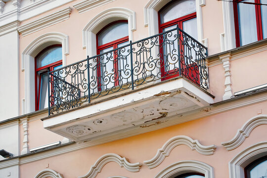 Old damaged balcony needs for repair, plaster chunks fall off. Balcony and facade with cracked plaster and paint, facade renovation. Risk of falling plaster, stucco or concrete pieces on pedestrians