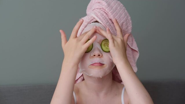 a little girl makes a mask on her face with cucumbers. Home spa