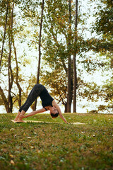 A fit yogi woman is practicing yoga in the forest in the autumn. She is in the Downward-Facing Dog...
