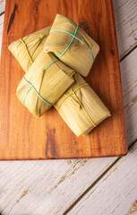 Pamonha, corn-based Brazilian food, arranged on a rustic wooden table, top view.