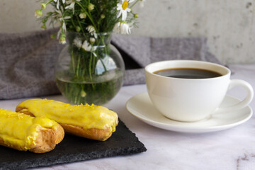 A white cup with black coffee and lemon eclairs on the table. Confectionery for sweet tooth.