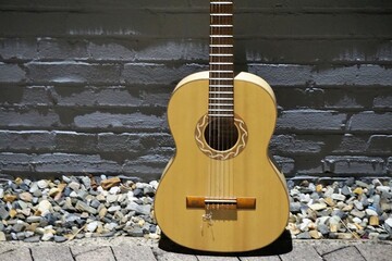 Goldgelbe Gitarre auf Kieselsteinboden vor grauer Backsteinwand 
