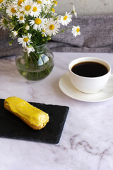 A white cup with black coffee and lemon eclairs on the table. Confectionery for sweet tooth.