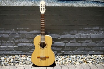 Goldgelbe Gitarre auf Kieselsteinboden vor grauer Backsteinfassade am Abend im Sommer