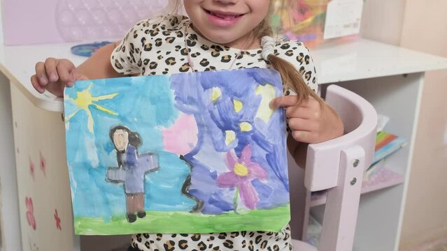 Talented Creative Child Girl Female Artist Draws Ranbow Mother summer on Paper, Child showing her work.Creates Colorful, Kid Drawing on table at Home. Painter Creating Abstract Modern Art. Childhood