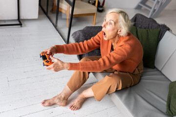 Attractive senior woman with grey hair playing console at home, having fun. Concept of mature...