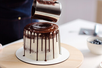 The confectioner decorates the cake with hot chocolate. The chocolate flows nicely over the cake. Close-up on a cake. High quality photo